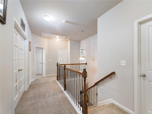 corridor with attic access, an upstairs landing, light colored carpet, and baseboards