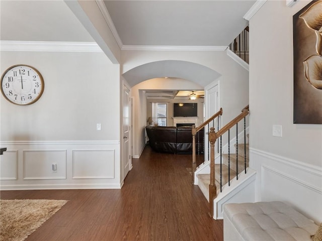 entrance foyer featuring wood finished floors, stairway, arched walkways, a fireplace, and crown molding