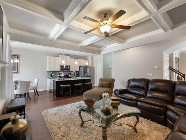 living area with a ceiling fan, coffered ceiling, dark wood finished floors, beam ceiling, and arched walkways