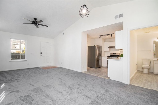 unfurnished living room featuring visible vents, a ceiling fan, light colored carpet, rail lighting, and vaulted ceiling