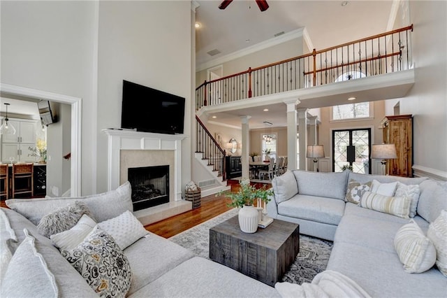 living area with a high end fireplace, wood finished floors, ornate columns, and ornamental molding