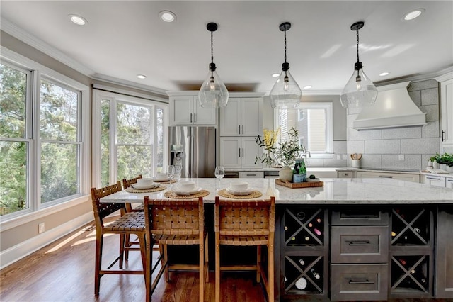 kitchen with a wealth of natural light, stainless steel fridge, crown molding, and custom range hood