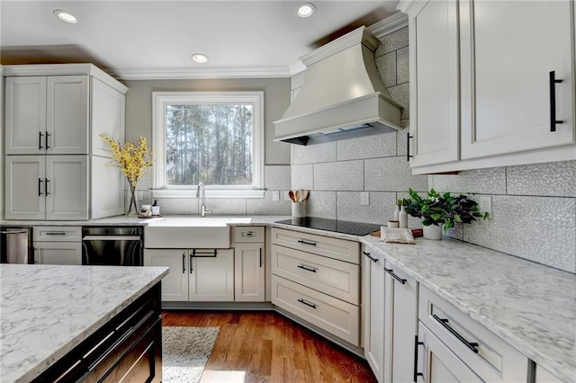 kitchen with black appliances, a sink, backsplash, wood finished floors, and custom exhaust hood