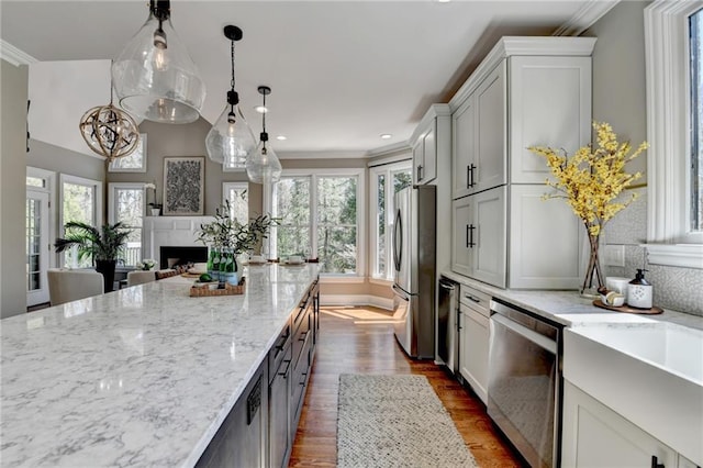 kitchen featuring ornamental molding, light stone counters, appliances with stainless steel finishes, a fireplace, and dark wood-style floors