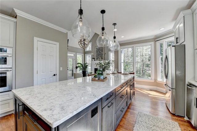 kitchen with light stone counters, a spacious island, light wood-style floors, appliances with stainless steel finishes, and crown molding