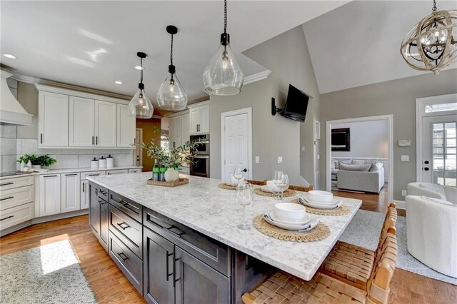 kitchen with light stone counters, tasteful backsplash, double oven, white cabinets, and light wood finished floors