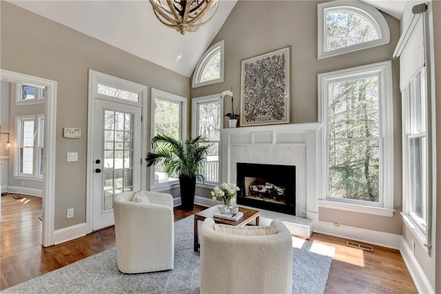 living area featuring wood finished floors, baseboards, visible vents, high vaulted ceiling, and a premium fireplace