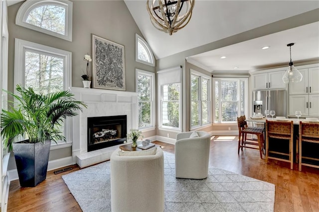 living room with visible vents, baseboards, light wood-style flooring, a fireplace, and high vaulted ceiling