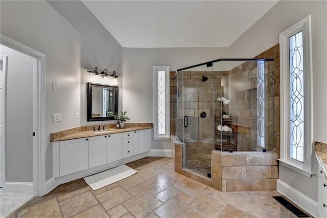 full bath with stone tile flooring, a stall shower, vanity, and baseboards