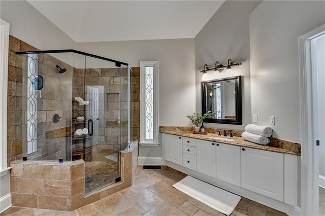 full bath featuring baseboards, vanity, stone tile flooring, and a shower stall