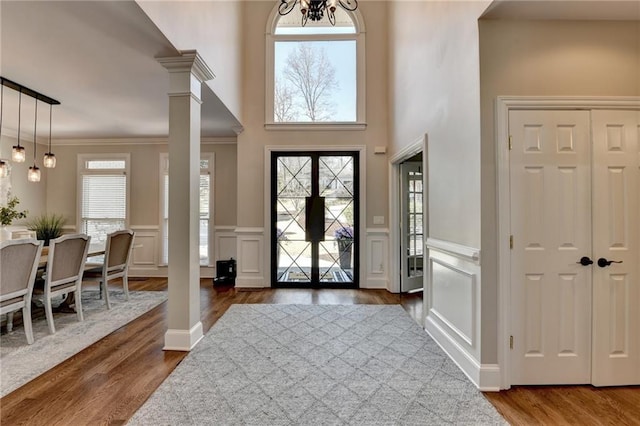 entryway with crown molding, a decorative wall, a chandelier, dark wood-style flooring, and ornate columns