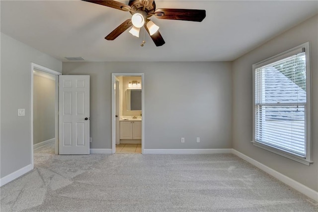 unfurnished bedroom featuring light colored carpet, ensuite bathroom, baseboards, and ceiling fan