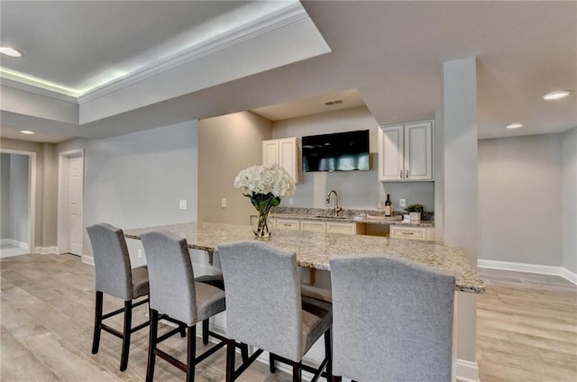 kitchen featuring a kitchen bar, light wood-style flooring, light stone countertops, and baseboards