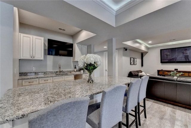 kitchen with visible vents, a sink, white cabinets, crown molding, and open floor plan