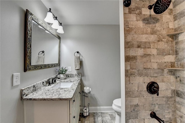 bathroom with baseboards, tiled shower, toilet, and vanity