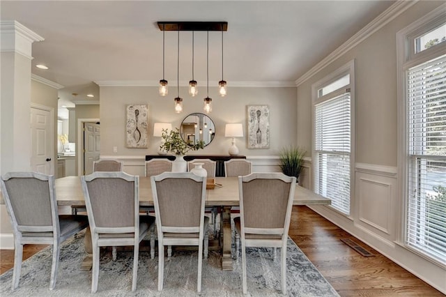 dining space featuring visible vents, crown molding, a wainscoted wall, and wood finished floors