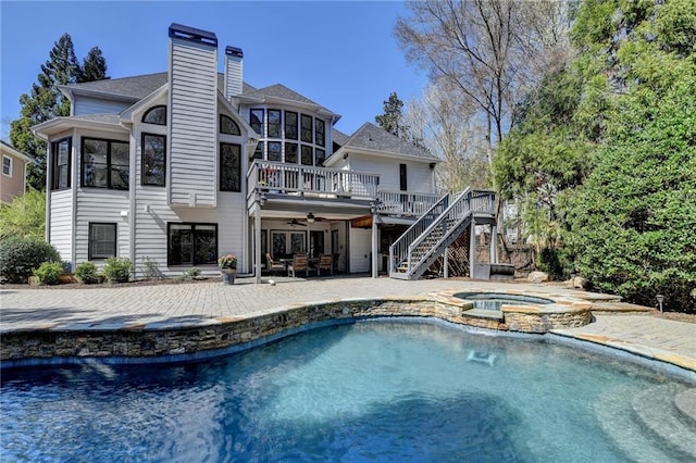 back of house with a pool with connected hot tub, stairs, a chimney, a deck, and a patio