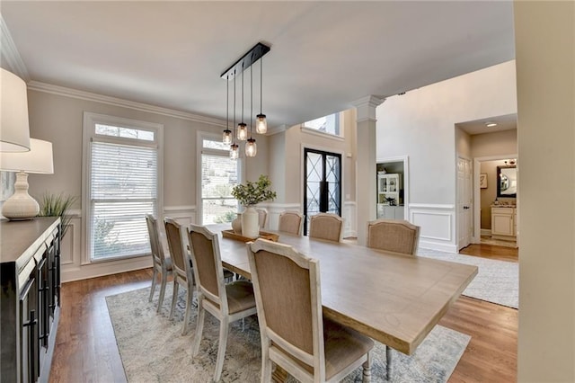 dining room featuring a wainscoted wall, light wood finished floors, ornamental molding, and ornate columns