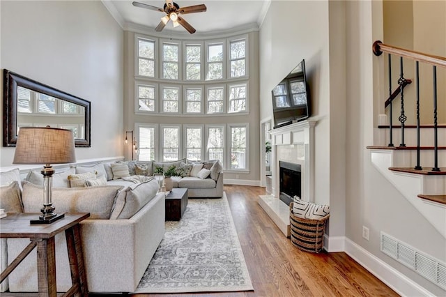 living area with visible vents, a towering ceiling, crown molding, and light wood finished floors