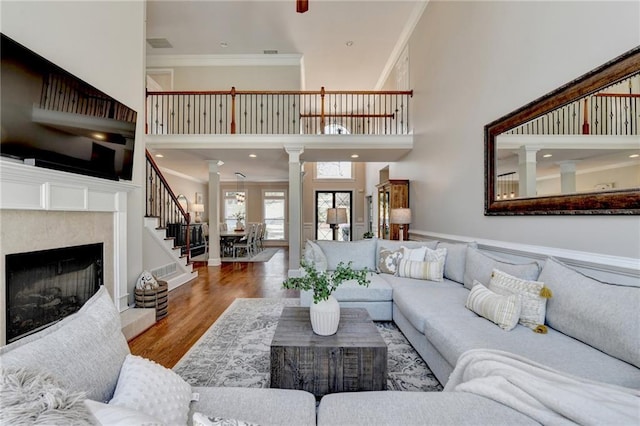 living area featuring a high end fireplace, ornamental molding, a towering ceiling, wood finished floors, and ornate columns