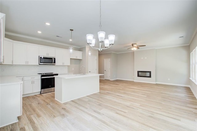 kitchen featuring appliances with stainless steel finishes, ceiling fan with notable chandelier, decorative light fixtures, white cabinets, and an island with sink