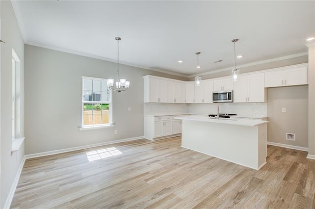 kitchen with backsplash, white cabinetry, a kitchen island with sink, and hanging light fixtures