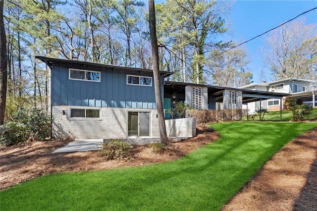 back of property with brick siding, board and batten siding, and a lawn