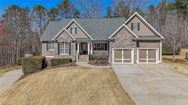 craftsman-style house with a front lawn, stone siding, covered porch, concrete driveway, and a garage