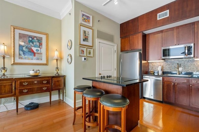 kitchen with a breakfast bar area, light wood-style flooring, stainless steel appliances, visible vents, and backsplash