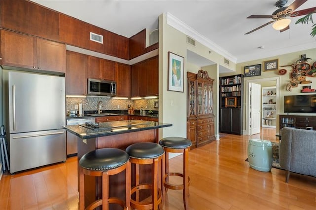 kitchen featuring stainless steel appliances, a breakfast bar, visible vents, light wood finished floors, and dark countertops