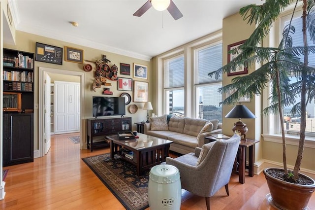 living room with light wood finished floors, ceiling fan, ornamental molding, and baseboards