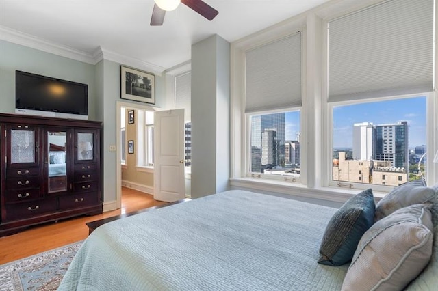 bedroom with a city view, crown molding, ceiling fan, ensuite bath, and wood finished floors