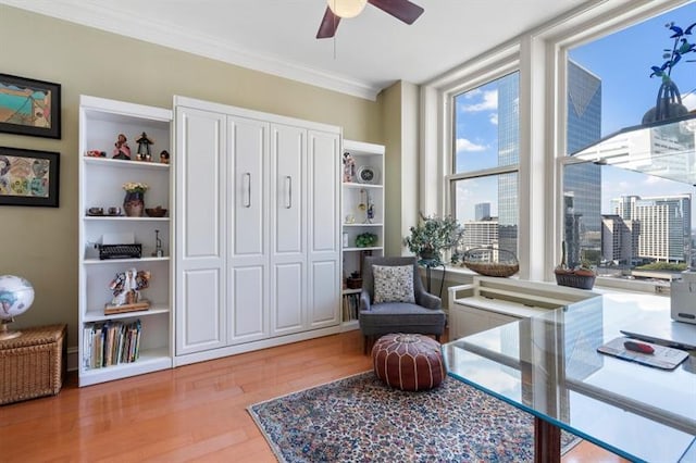 living area with light wood-style floors, ornamental molding, a wall of windows, and a ceiling fan