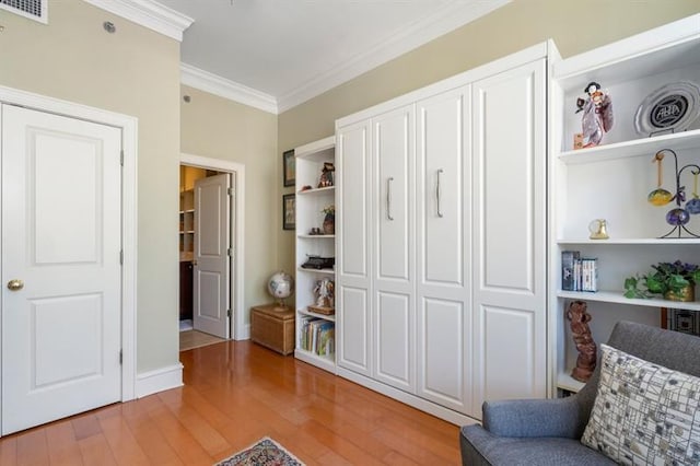 sitting room with light wood-type flooring, visible vents, and crown molding