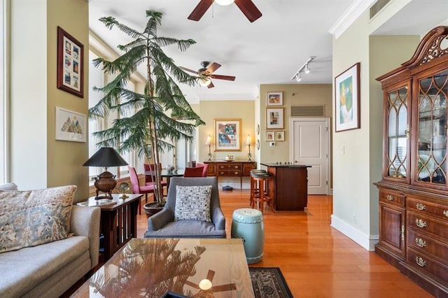 living area featuring visible vents, baseboards, ceiling fan, ornamental molding, and light wood-type flooring