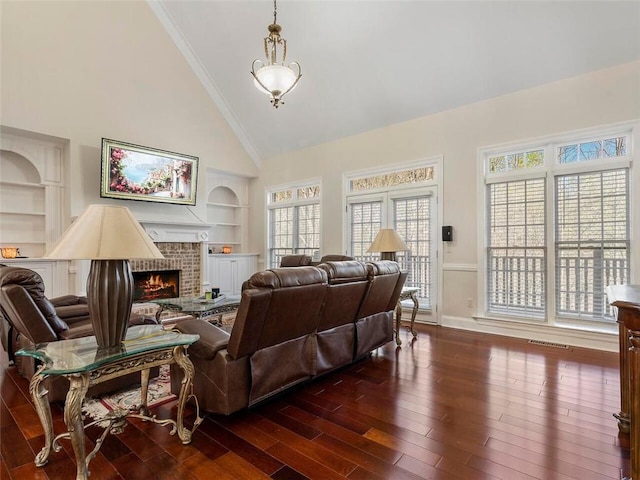 living room with a brick fireplace, high vaulted ceiling, dark hardwood / wood-style floors, ornamental molding, and built in shelves