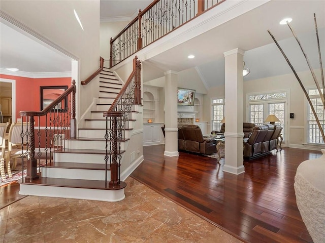 staircase with built in features, hardwood / wood-style floors, decorative columns, ornamental molding, and high vaulted ceiling