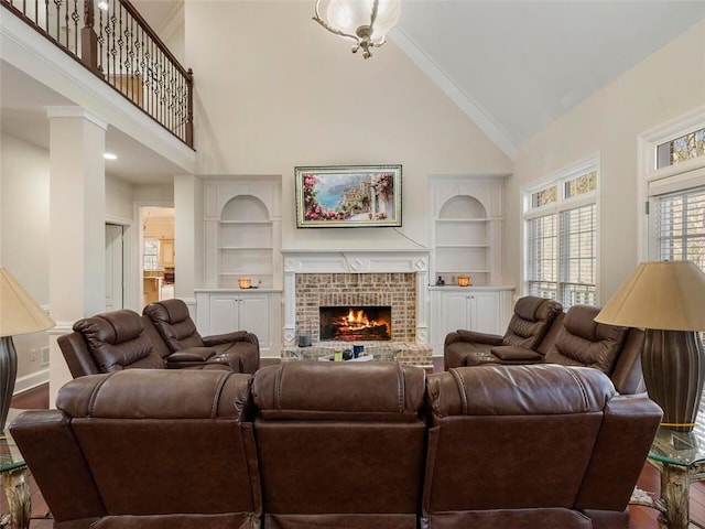 living room featuring a brick fireplace, high vaulted ceiling, crown molding, built in features, and decorative columns