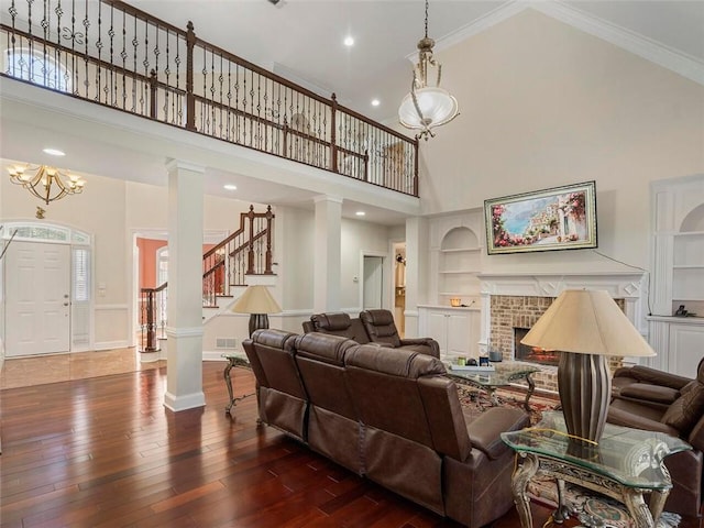 living room featuring dark wood-type flooring, a high ceiling, ornate columns, crown molding, and built in shelves