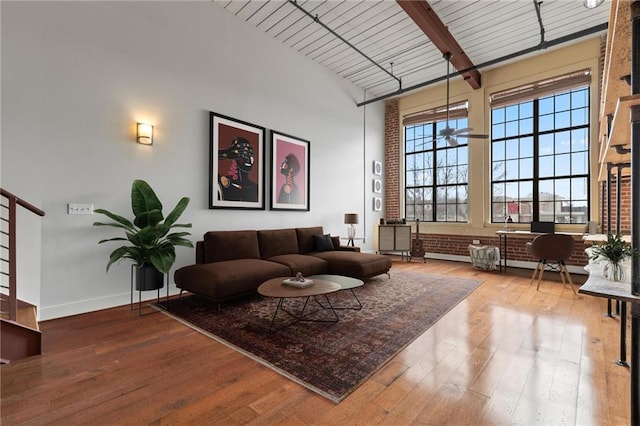 living area featuring baseboards, beamed ceiling, wood-type flooring, and a towering ceiling