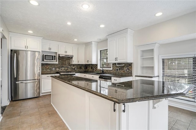 kitchen featuring white cabinetry, stainless steel appliances, a kitchen island, and dark stone counters