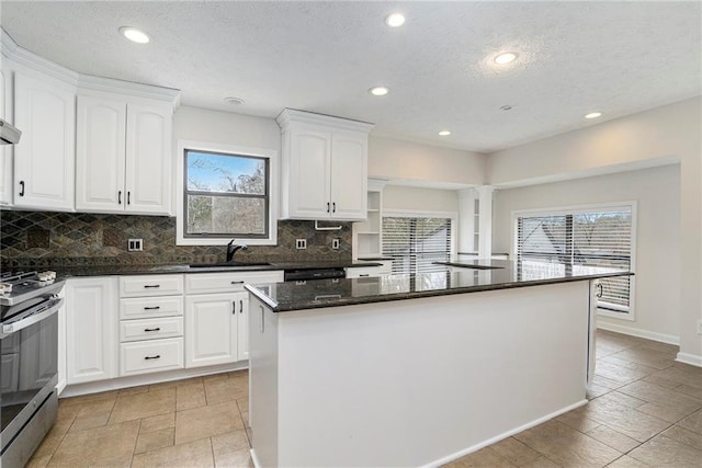 kitchen featuring sink, stainless steel gas range oven, white cabinetry, a center island, and dark stone counters