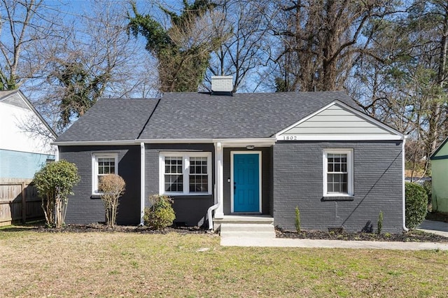 view of front of house featuring brick siding, a front lawn, a shingled roof, and fence