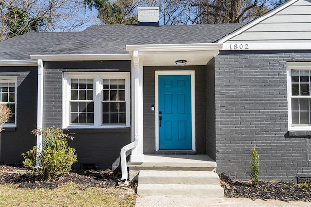 doorway to property with roof with shingles, a chimney, and brick siding