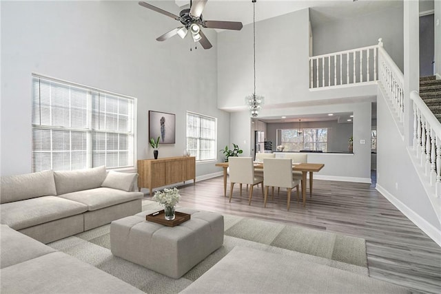 living area featuring a ceiling fan, stairway, baseboards, and wood finished floors