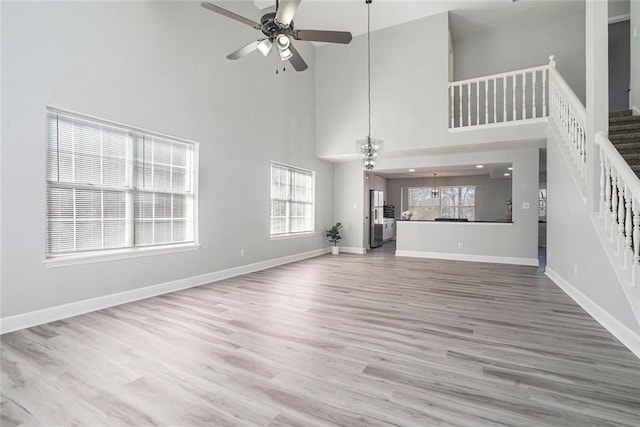 unfurnished living room featuring a ceiling fan, baseboards, stairway, and wood finished floors