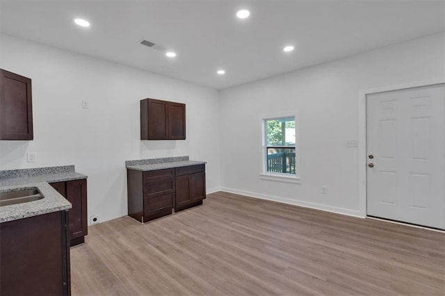 kitchen with light hardwood / wood-style floors, light stone counters, and dark brown cabinetry