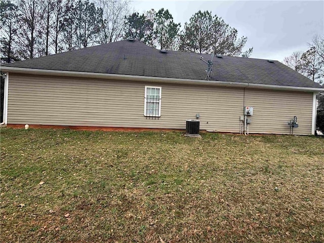 rear view of property with a lawn, cooling unit, and roof with shingles