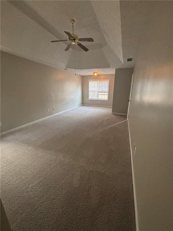 unfurnished room featuring a textured ceiling, carpet floors, a ceiling fan, baseboards, and a raised ceiling