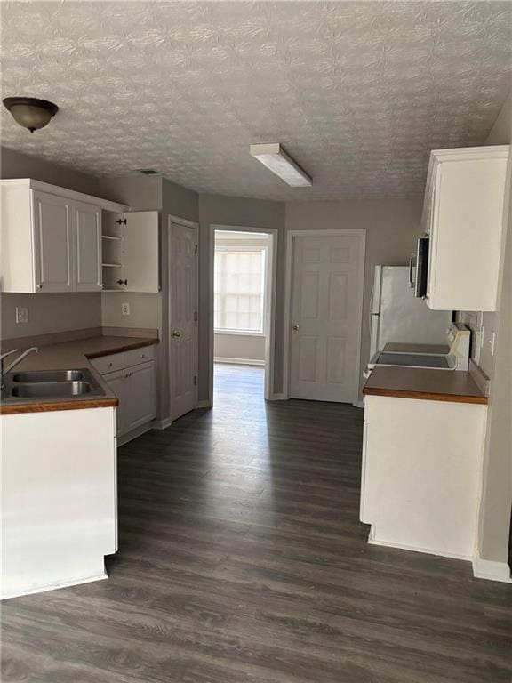 kitchen with dark wood finished floors, open shelves, white cabinetry, a sink, and baseboards